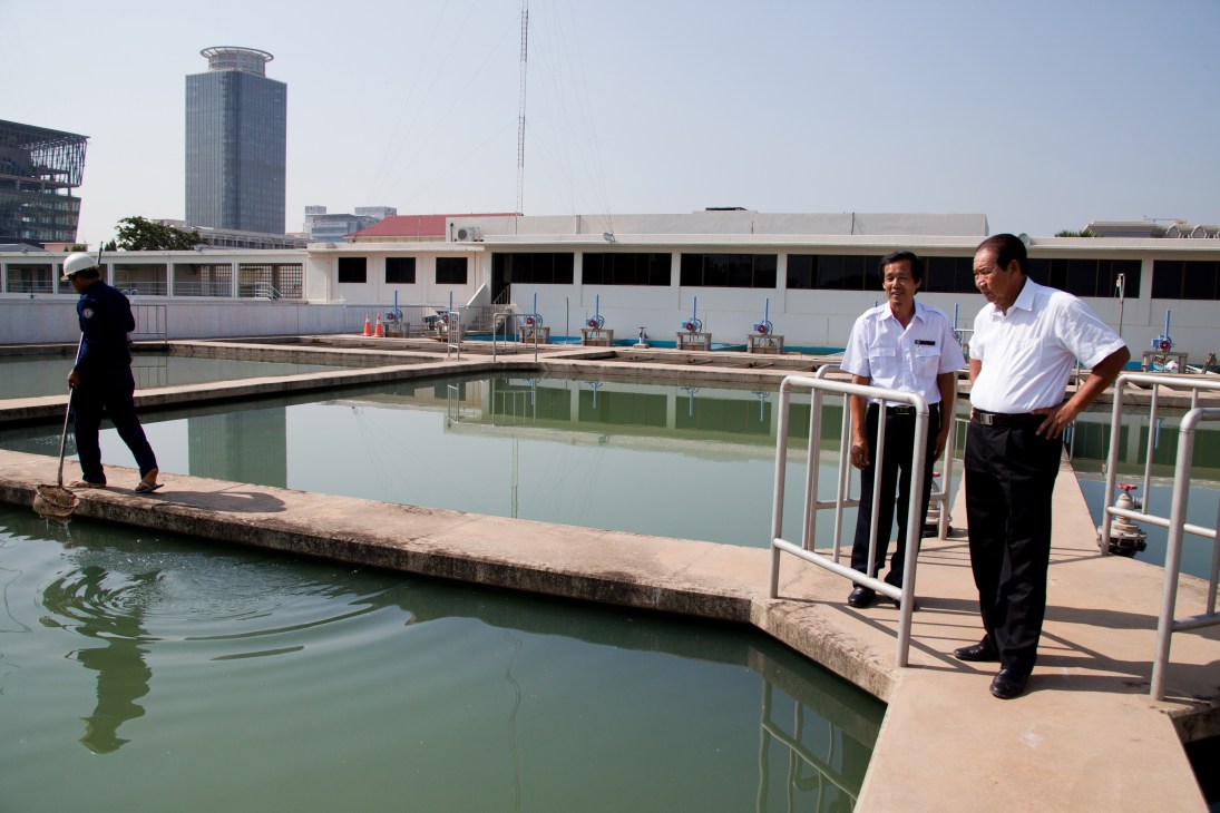Two men in white shirts stand on a platform overlooking water treatment facilities in Phnom Penh.