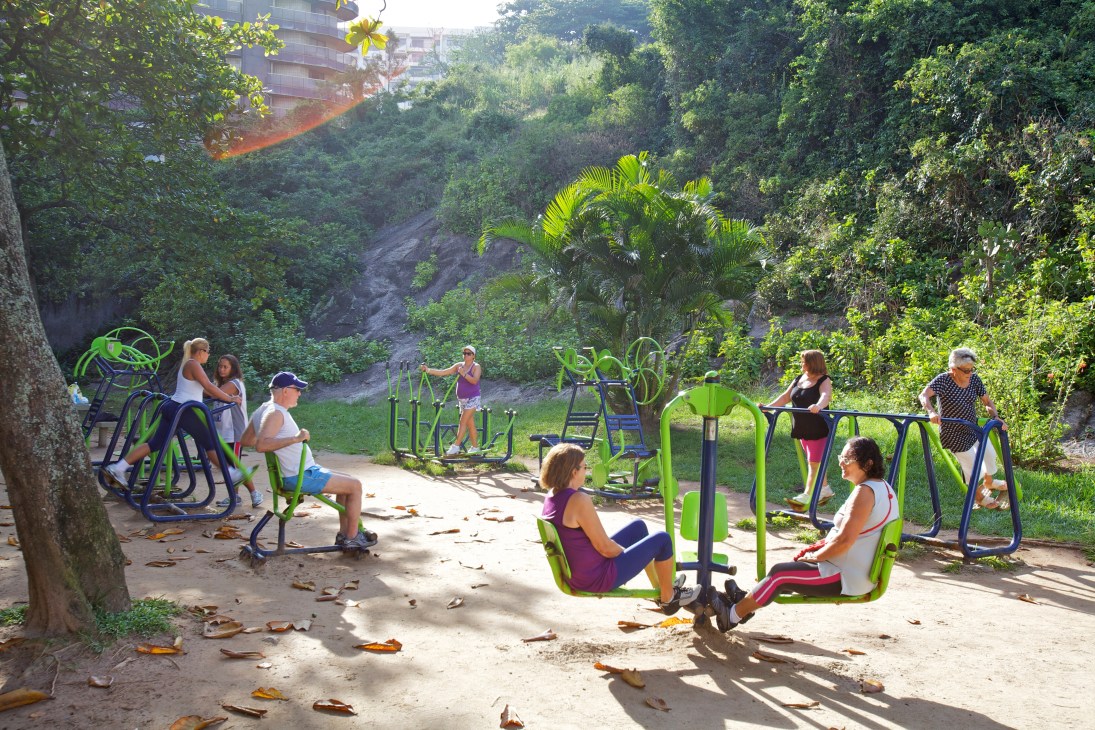 People using outdoor exercise equipment in a leafy Rio de Janeiro park with tropical vegetation.