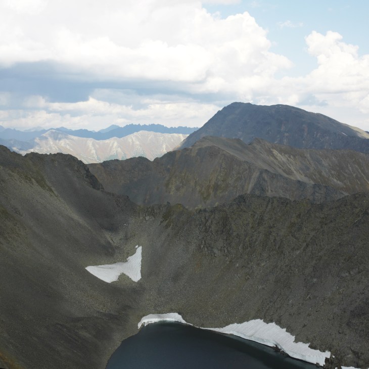 Snow-capped volcanic peaks and ridges rise above a dark mountain lake in central Kamchatka.