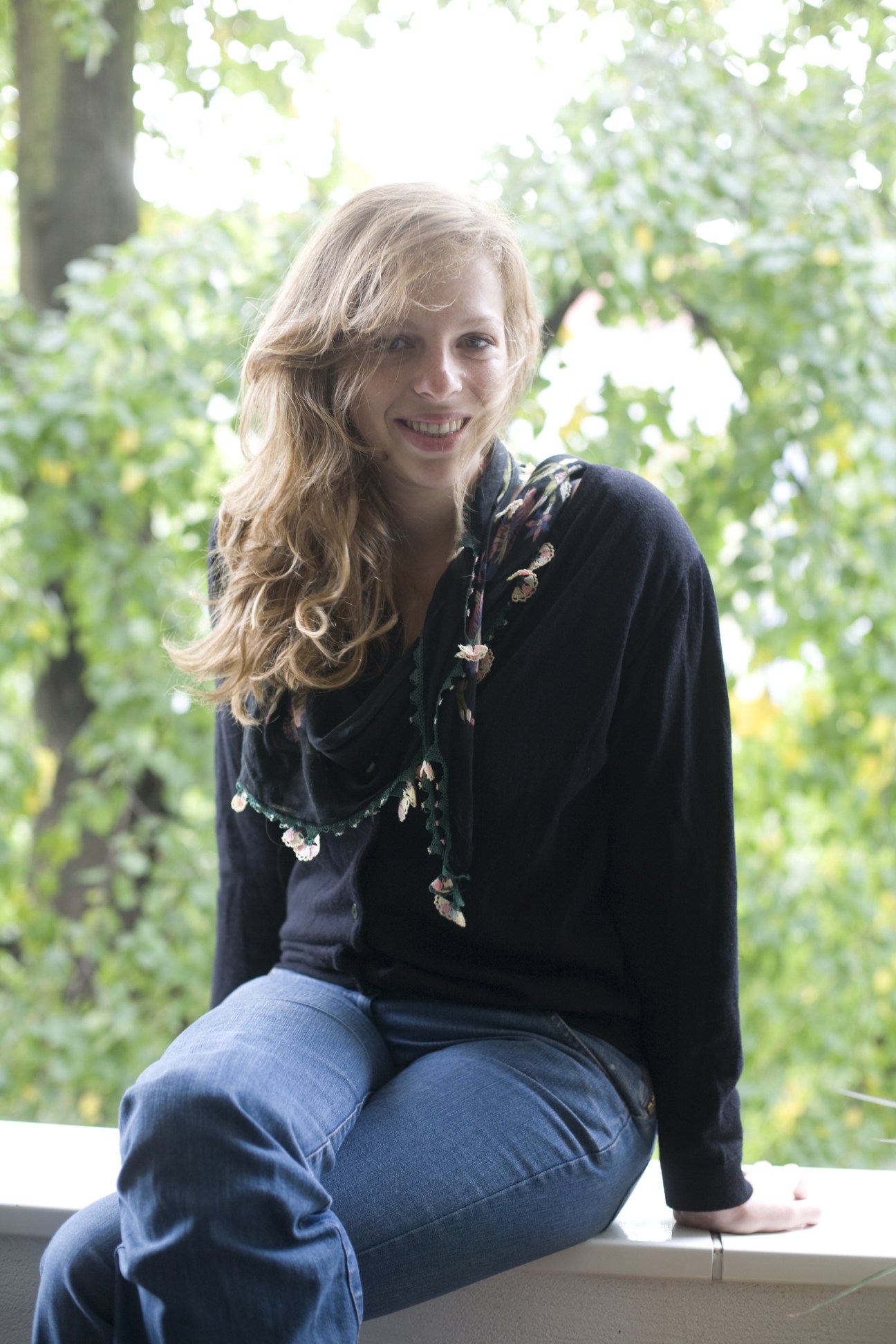 Charly Wilder, a journalist, smiles at the camera while sitting outdoors surrounded by green foliage.