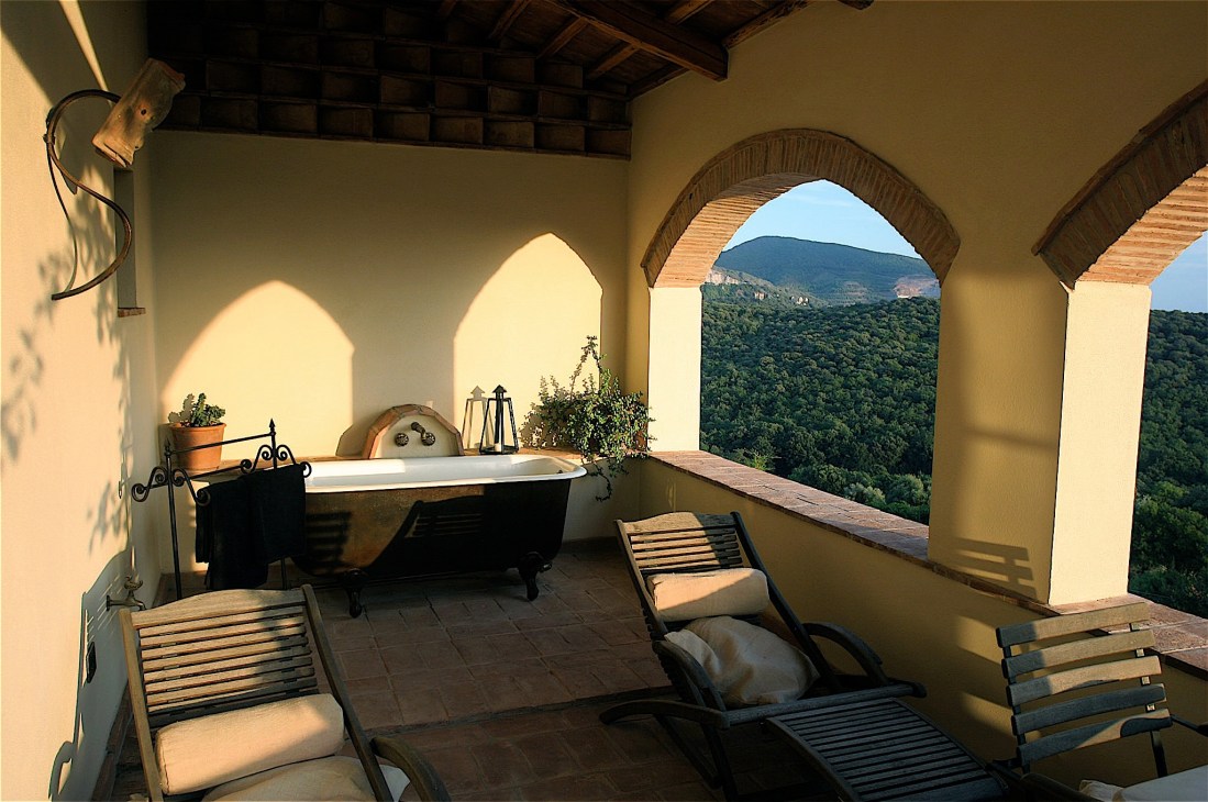 Terrace with bathtub and lounge chairs overlooking forested Tuscan hills at Poggio ai Santi.