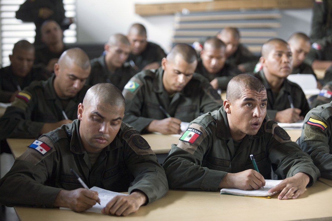 Police officers from multiple Latin American countries sit at desks during a classroom instruction session.