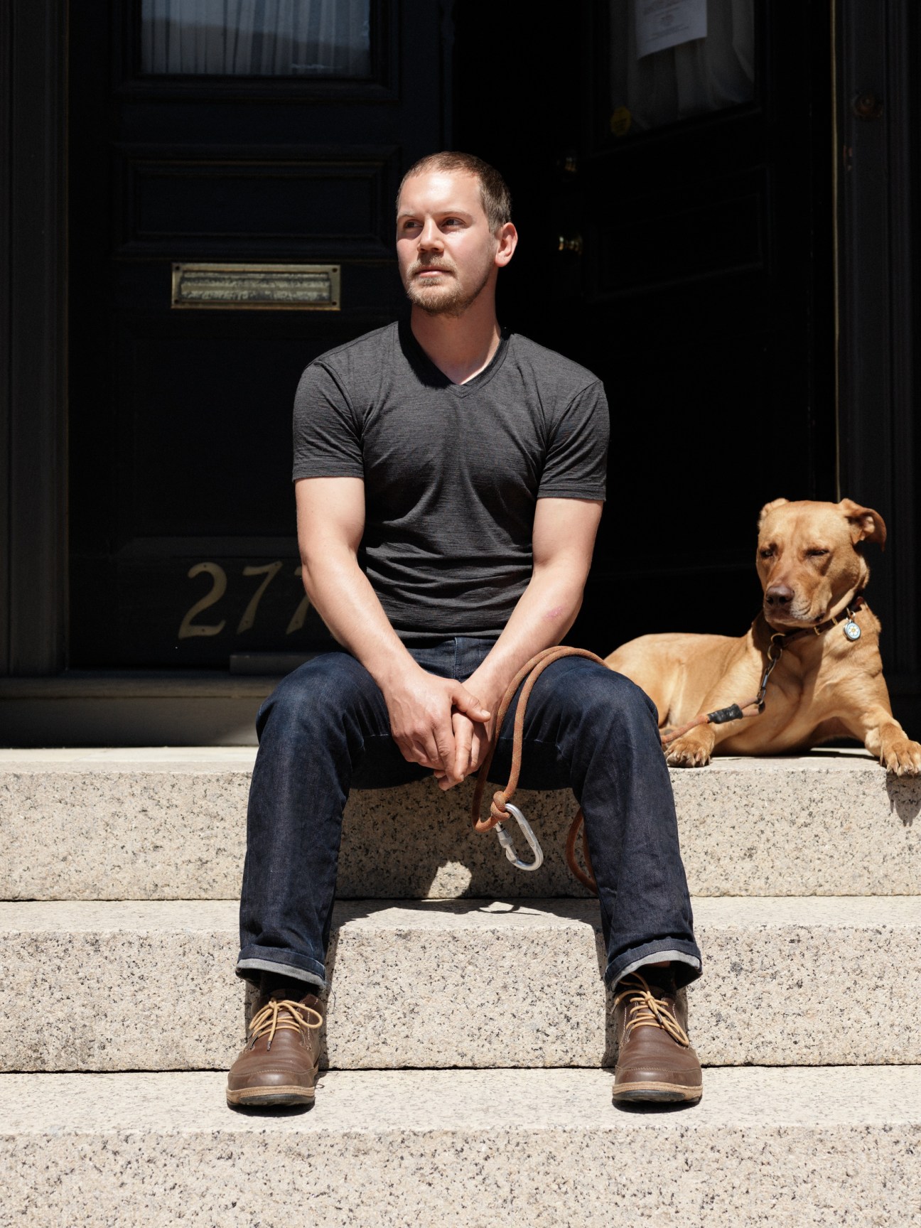 Man sitting on house steps with brown dog on sunny day in Portland.