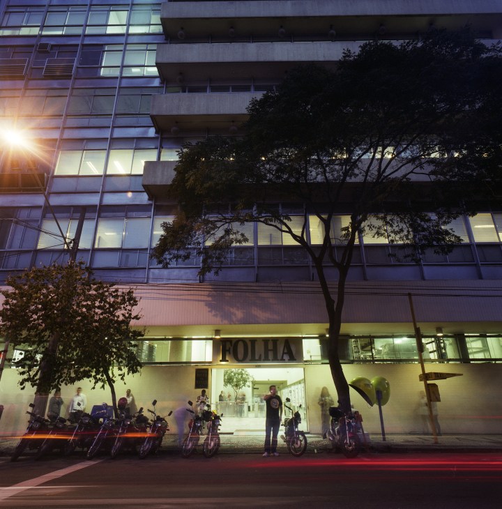 Folha de S.Paulo headquarters entrance at dusk with illuminated storefront and motorcycles parked outside.