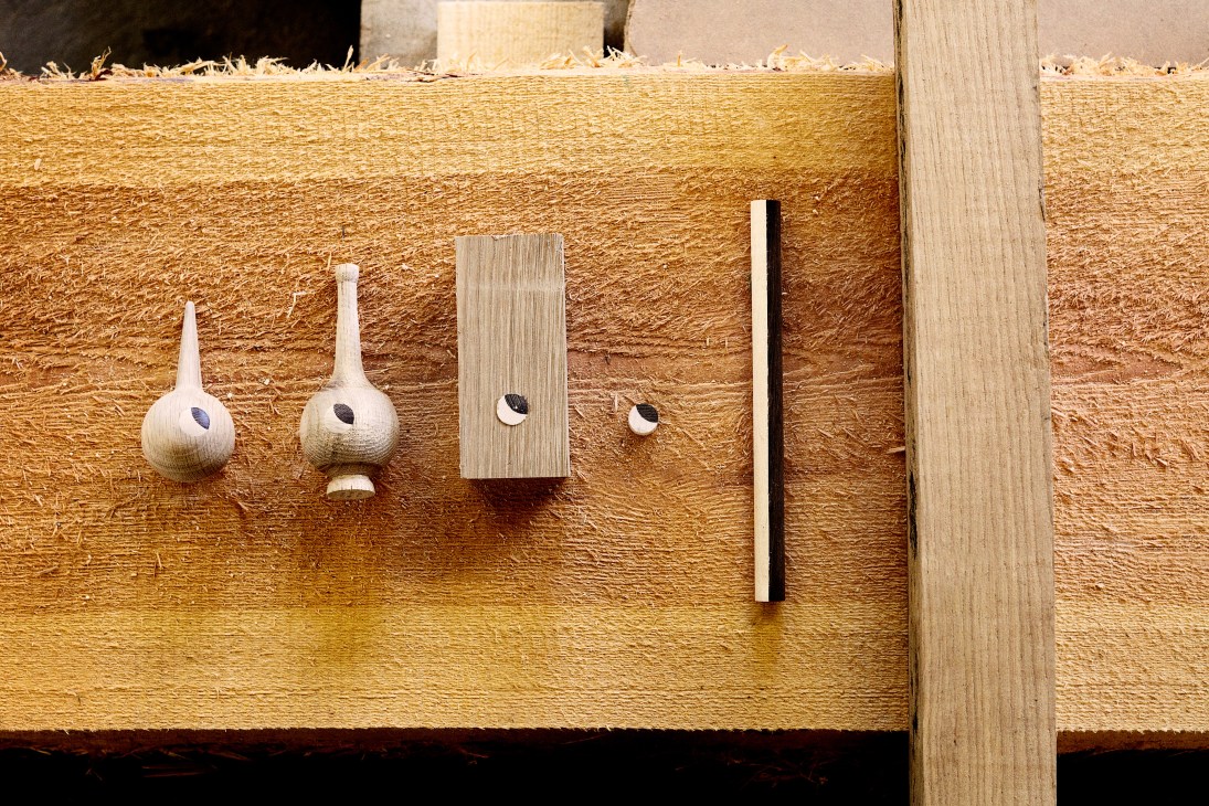 Wooden bird head designs with eyes being applied, displayed on a textured wooden surface.