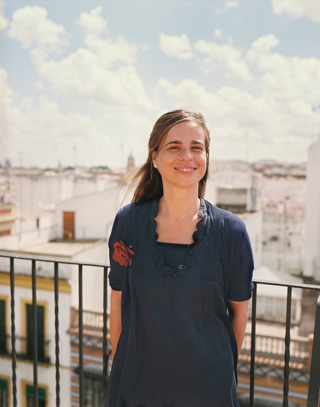 Woman smiling on a rooftop terrace overlooking Seville's white buildings and cityscape.