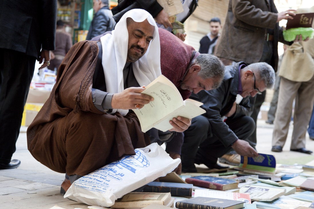 Man in white headscarf browsing books at a street book sale on Muntanabi street in Baghdad.