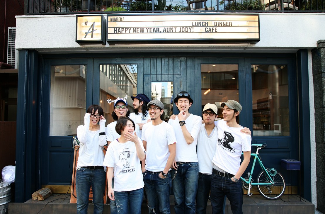 Team members in white t-shirts posing outside Number A diner in Tokyo with signage visible above.