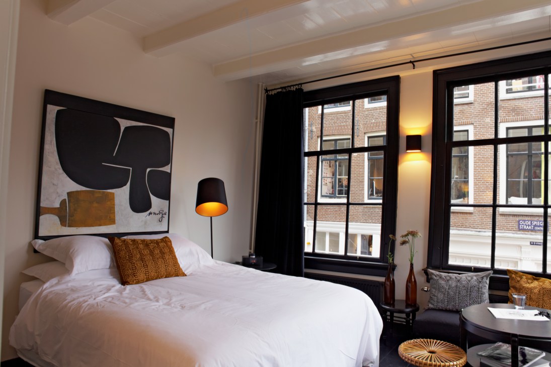 Modern bedroom at Maison Rika guesthouse in Amsterdam with white bedding, abstract artwork, and canal-side windows.