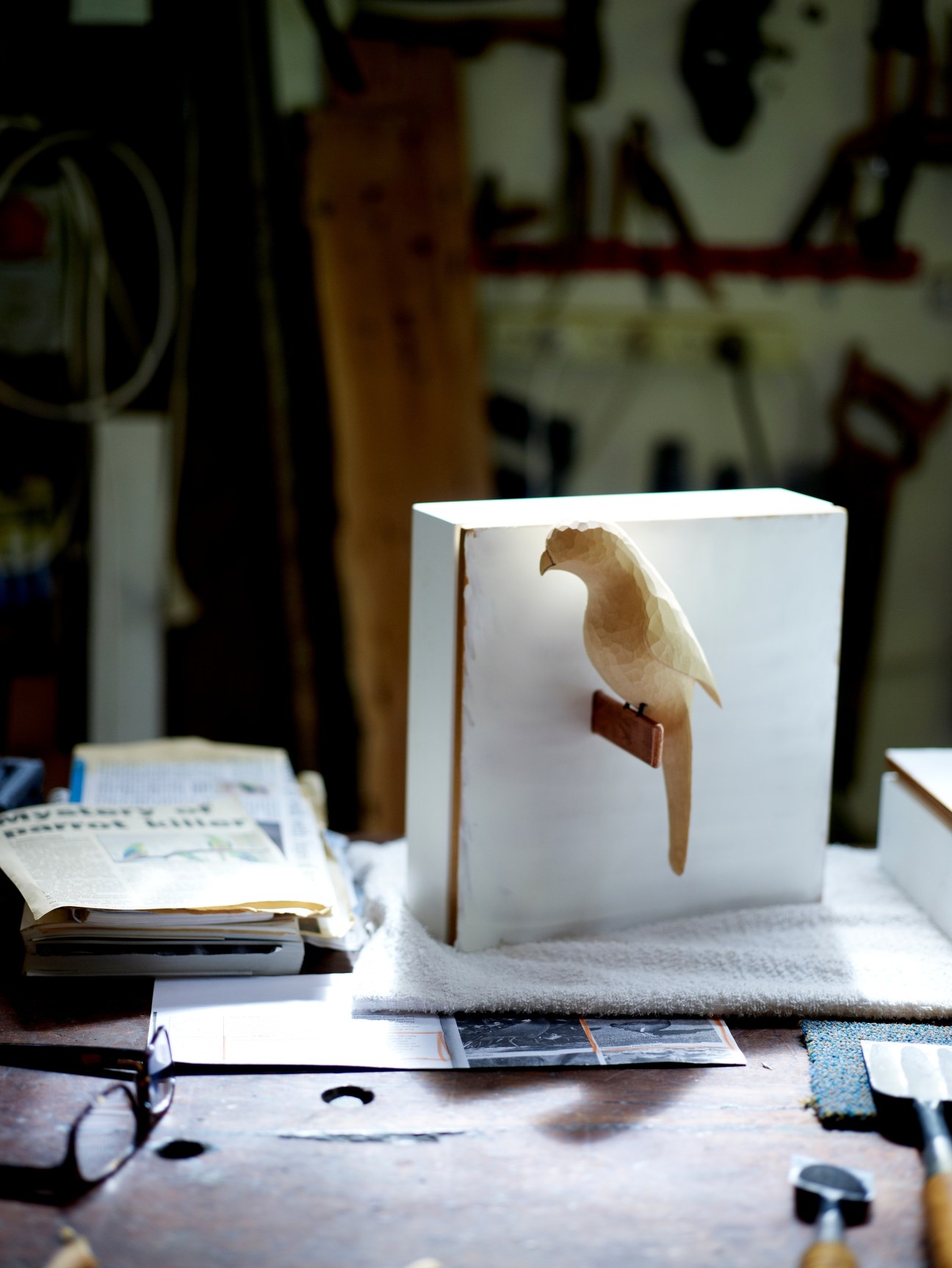 Wooden carved bird sculpture displayed on white box in a craftsman's workshop.
