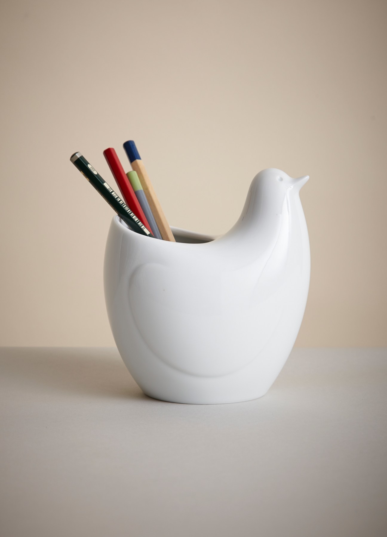 White ceramic bird-shaped container holding colored pencils and writing implements.