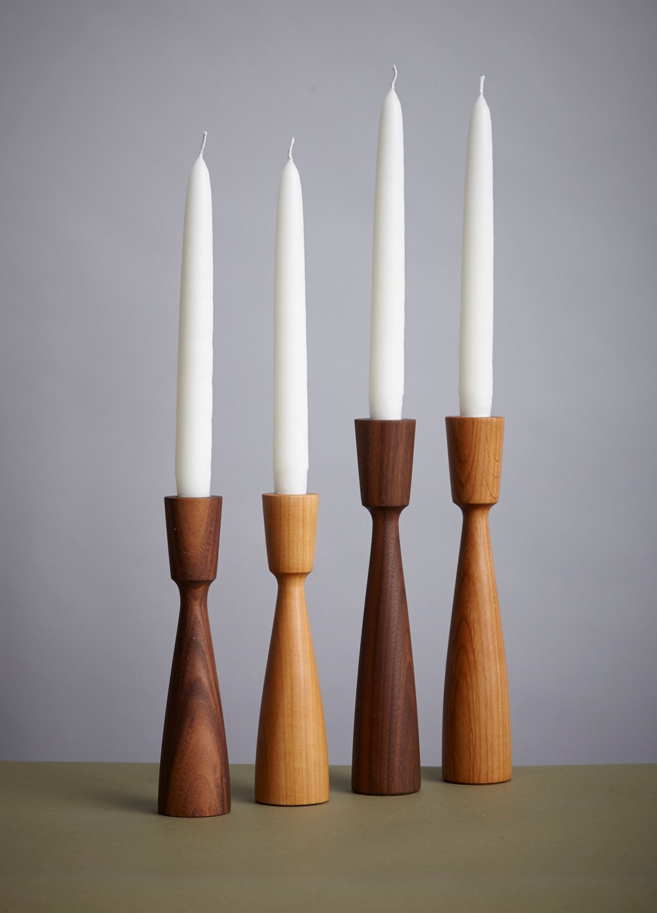 Four hand-turned wooden candlesticks in walnut and alder wood holding white taper candles.