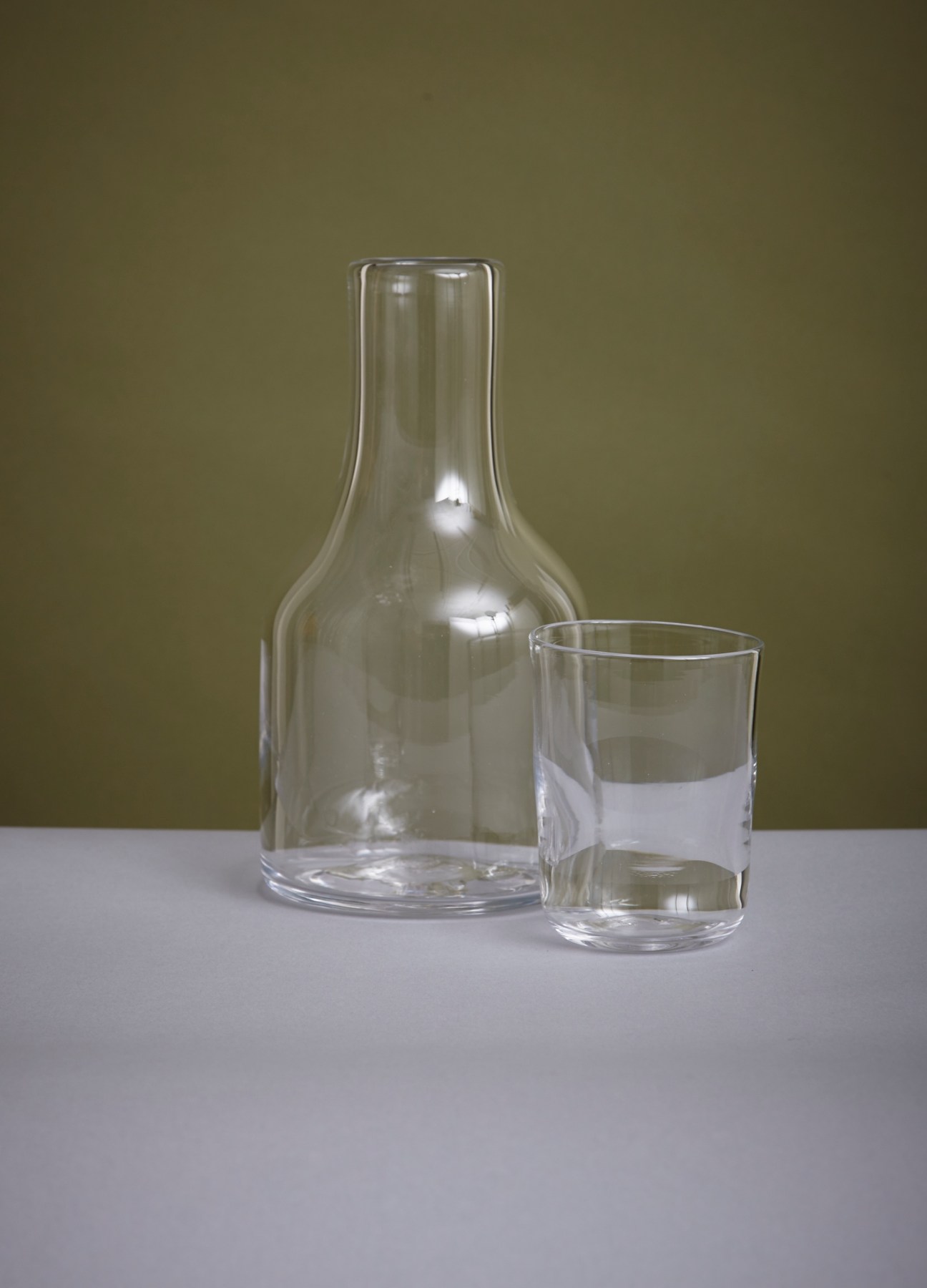 Clear glass carafe and drinking glass by Jerpoint Glass Studio, displayed against a muted green background.