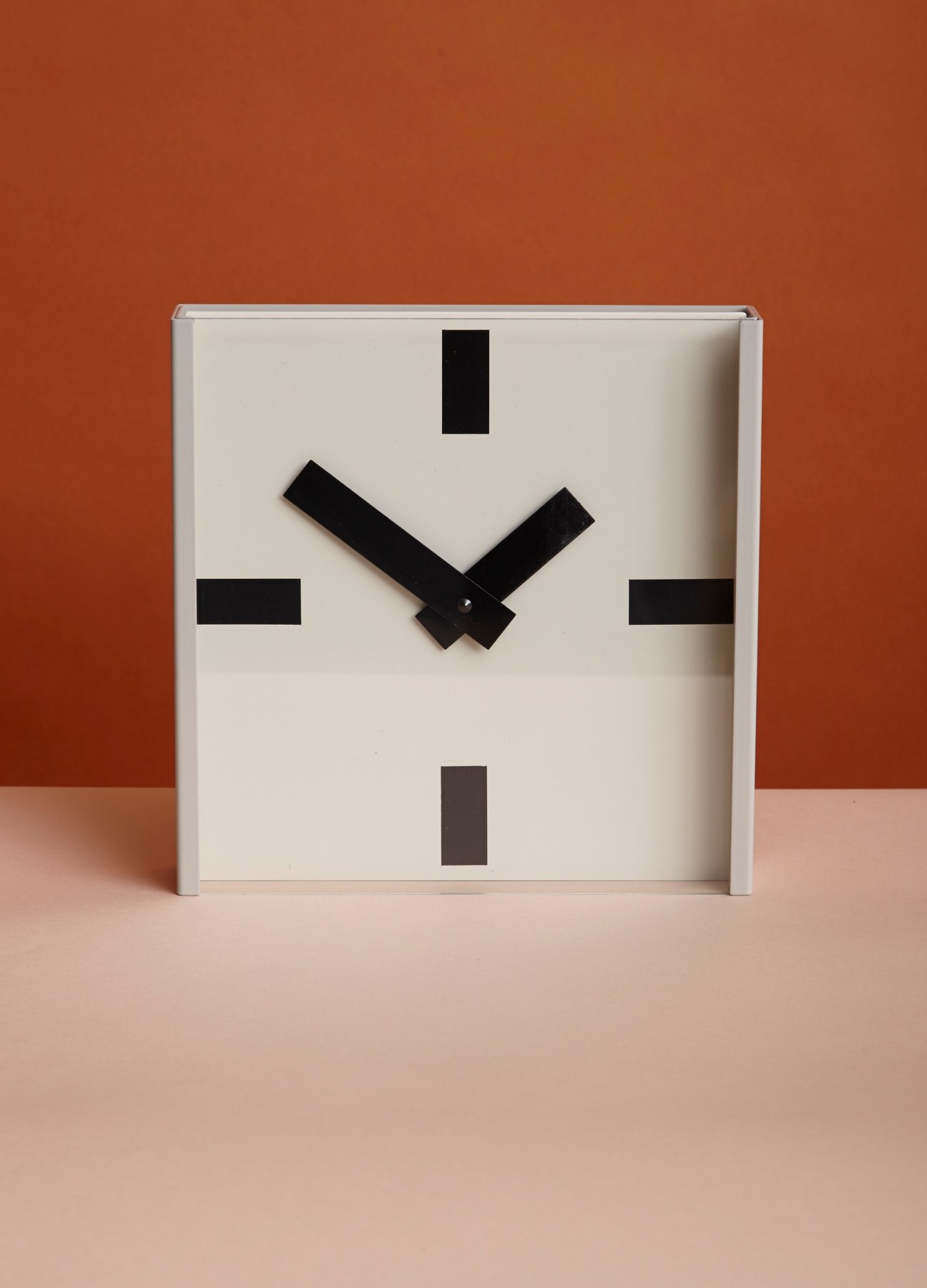 Minus tio Twenty Four Hours steel and glass clock with geometric black hands on white face.