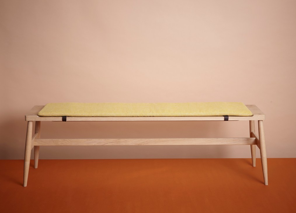 Light wood bench with yellow-green cushion against pink and orange background.