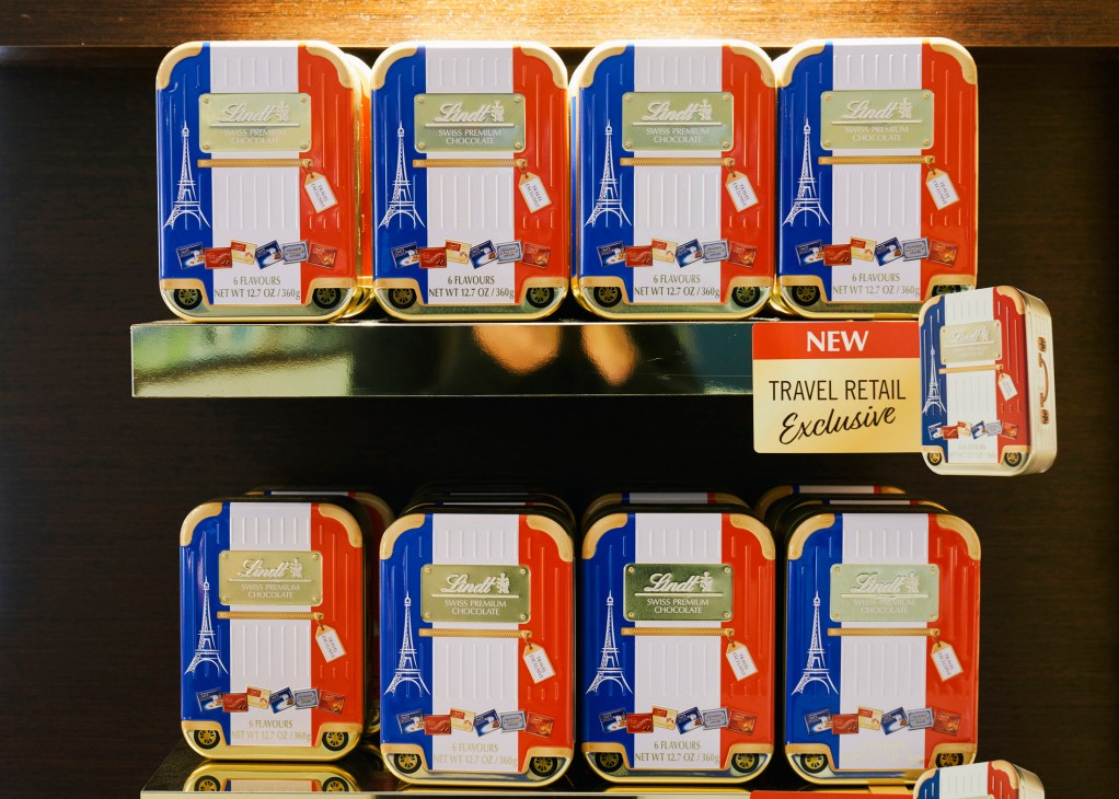 Display of Lindt Swiss premium chocolate gift tins with French flag design and Eiffel Tower graphics on store shelf