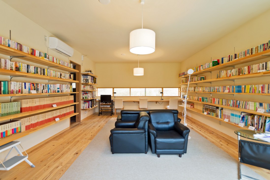 Library interior with wooden shelves lining walls, black leather chairs, and natural light from windows.