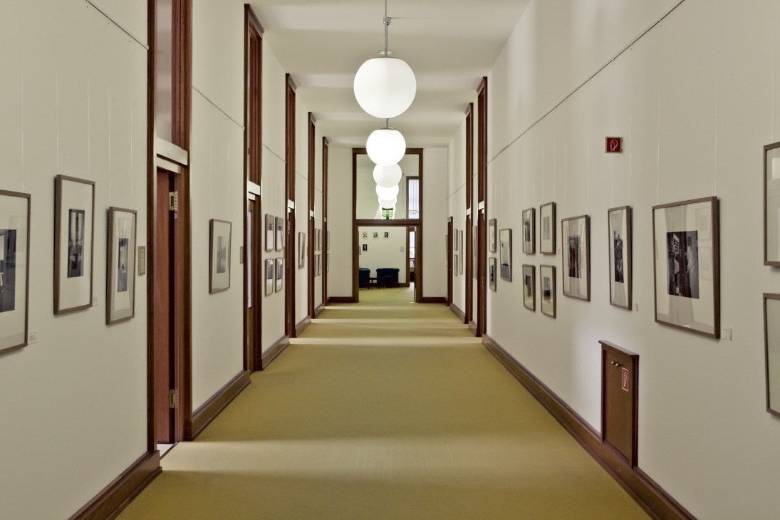 Long hallway with cream walls, dark wood-framed doors, and hanging spherical light fixtures.