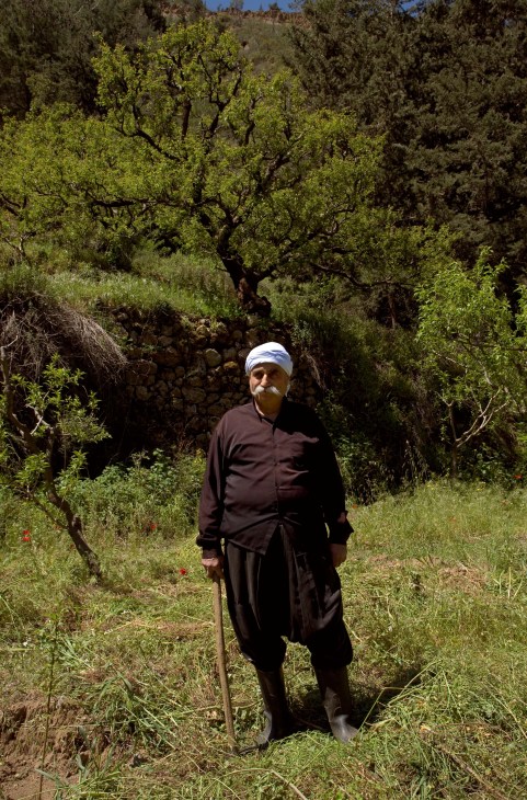 Druze farmer Nadeem Abi Ali stands in traditional black clothing and white headwrap among olive trees in a Lebanese orchard.