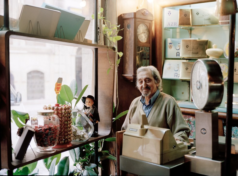 Mr Azrak stands in his patisserie surrounded by display cases with packaged goods and decorative items.