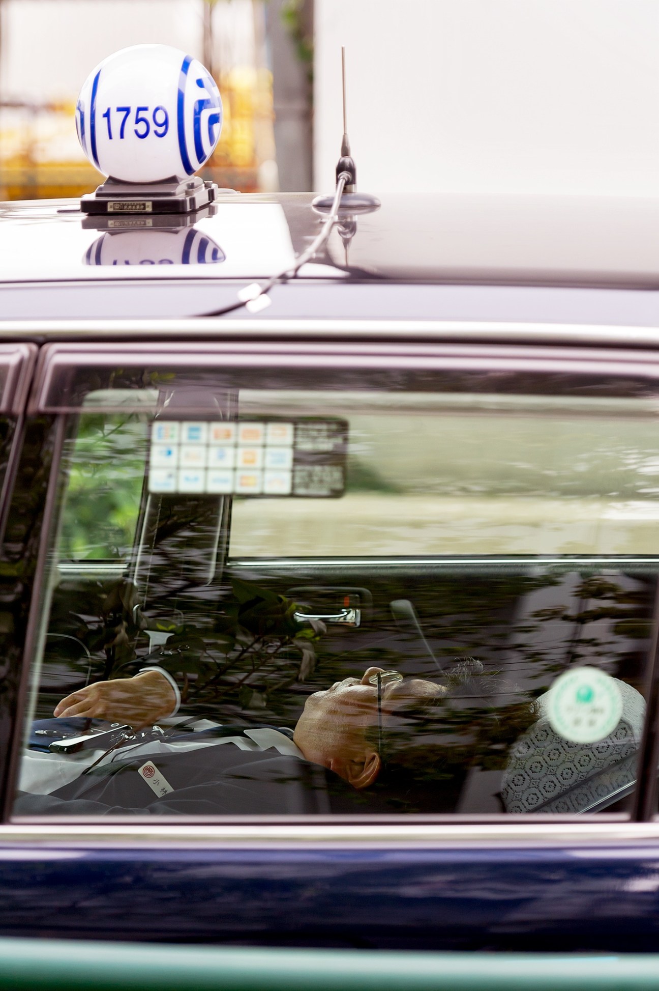 A Tokyo taxi driver rests in his vehicle during a shift break, with the illuminated taxi lamp displaying number 1759 visible on the roof.