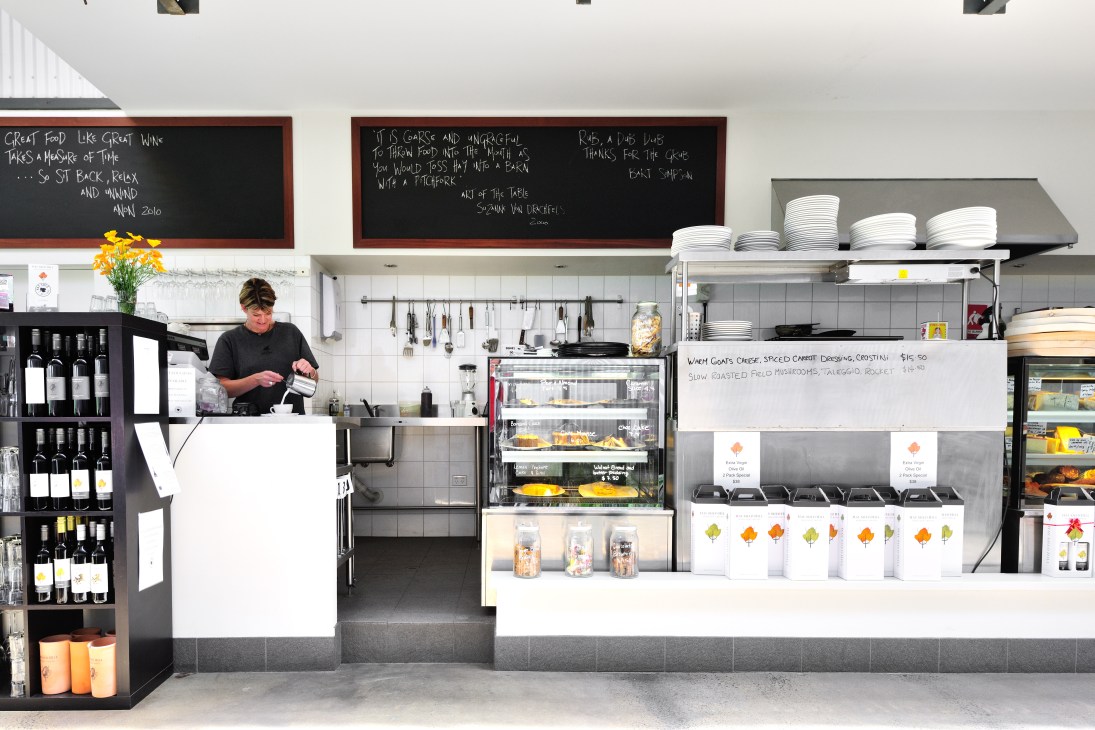 Chef working at counter in modern minimalist café kitchen with white plates and menu boards.