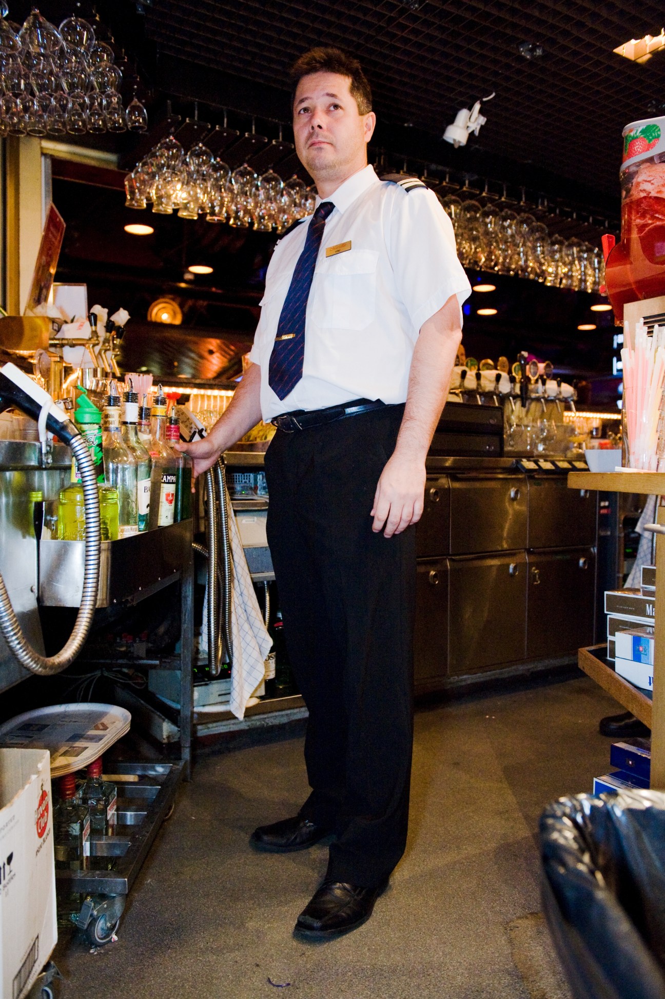 Head barman Arne Schreck stands behind a bar on M/S Gabriella ferry, wearing a white shirt and navy tie.