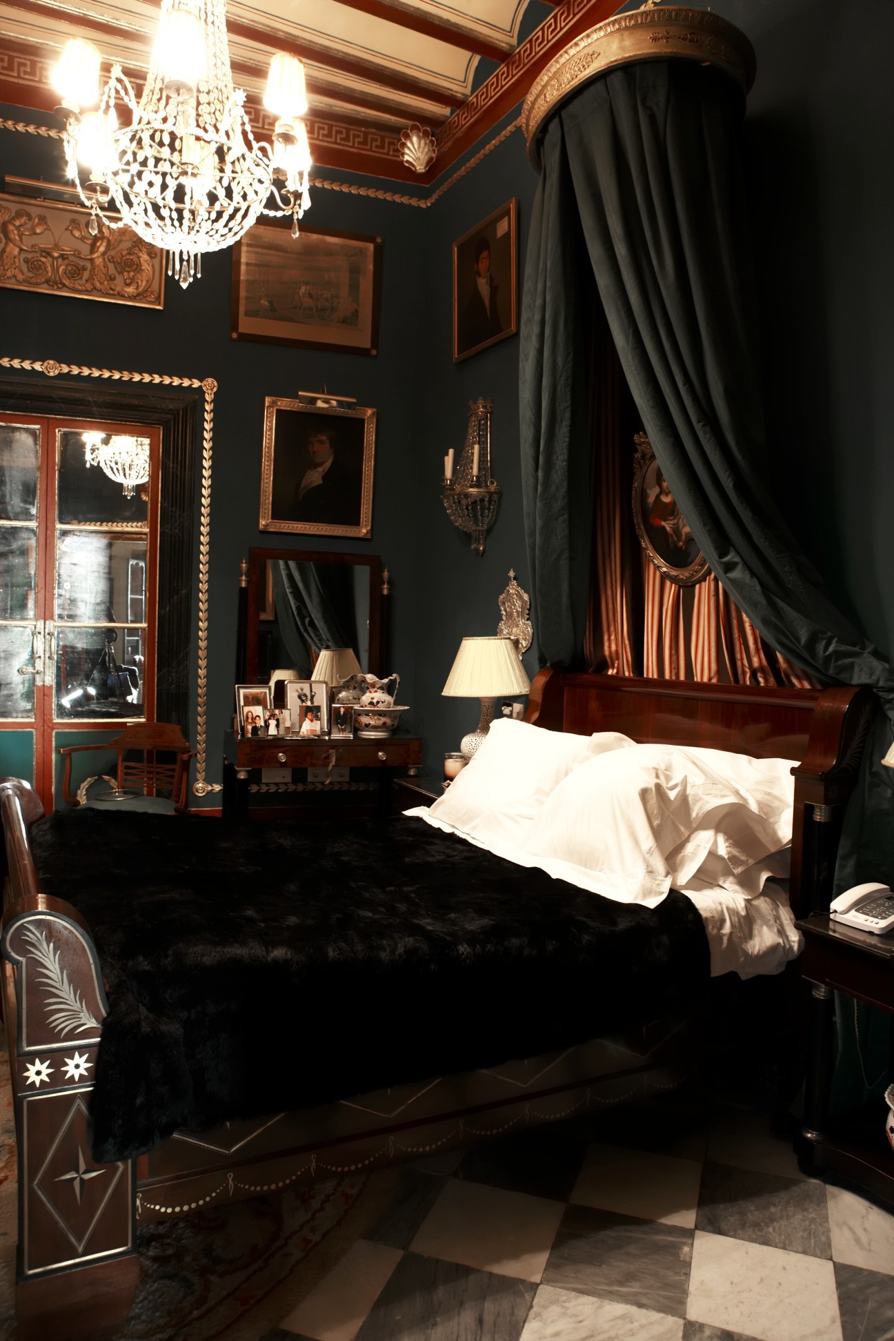 Luxurious bedroom with dark walls, ornate crystal chandelier, wooden canopy bed with black curtains, and period furnishings in La Bella Escondida.
