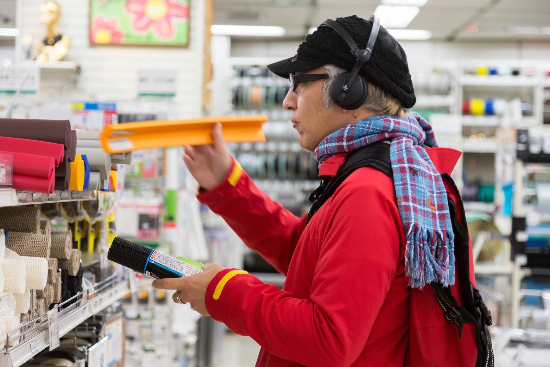 Customer wearing headphones and red jacket browsing colorful storage bins in DIY Creative Materials section.