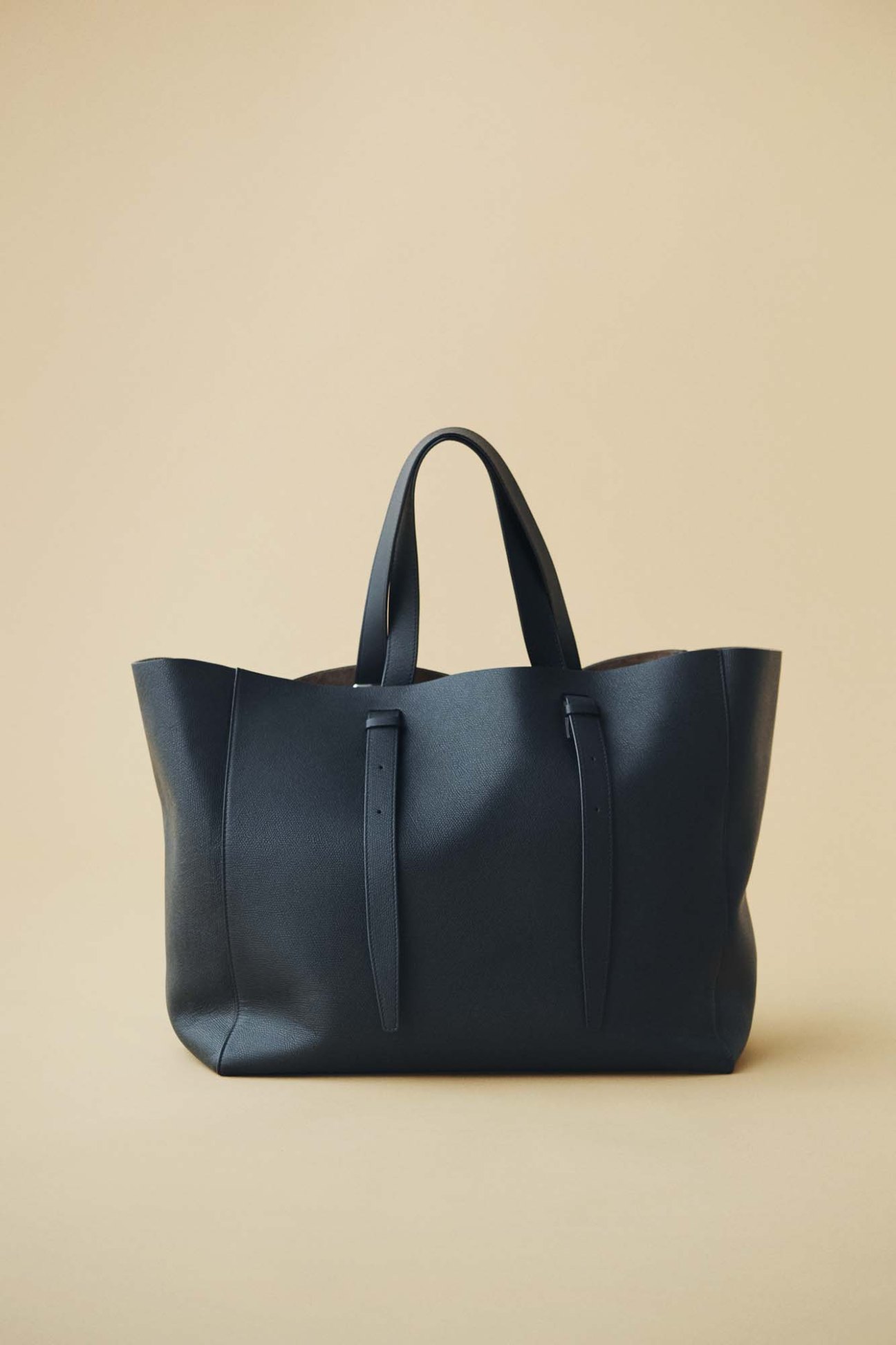 Black leather tote bag by Valextra with dual handles on cream background