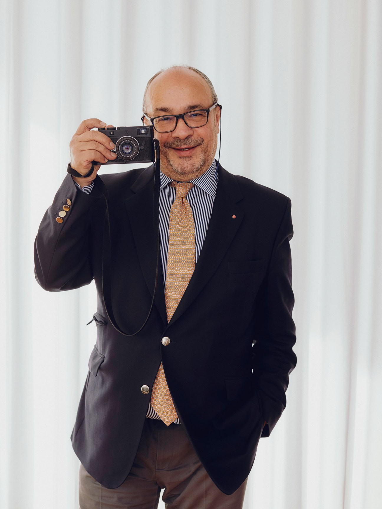 Andreas Kaufmann, Leica's managing director, holds a vintage Leica camera while wearing a dark blazer and striped shirt.