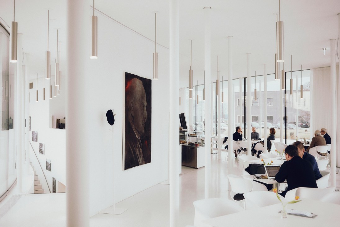 Workers gather at tables in a bright, minimalist cafeteria with pendant lighting and large windows overlooking Leitz Park.