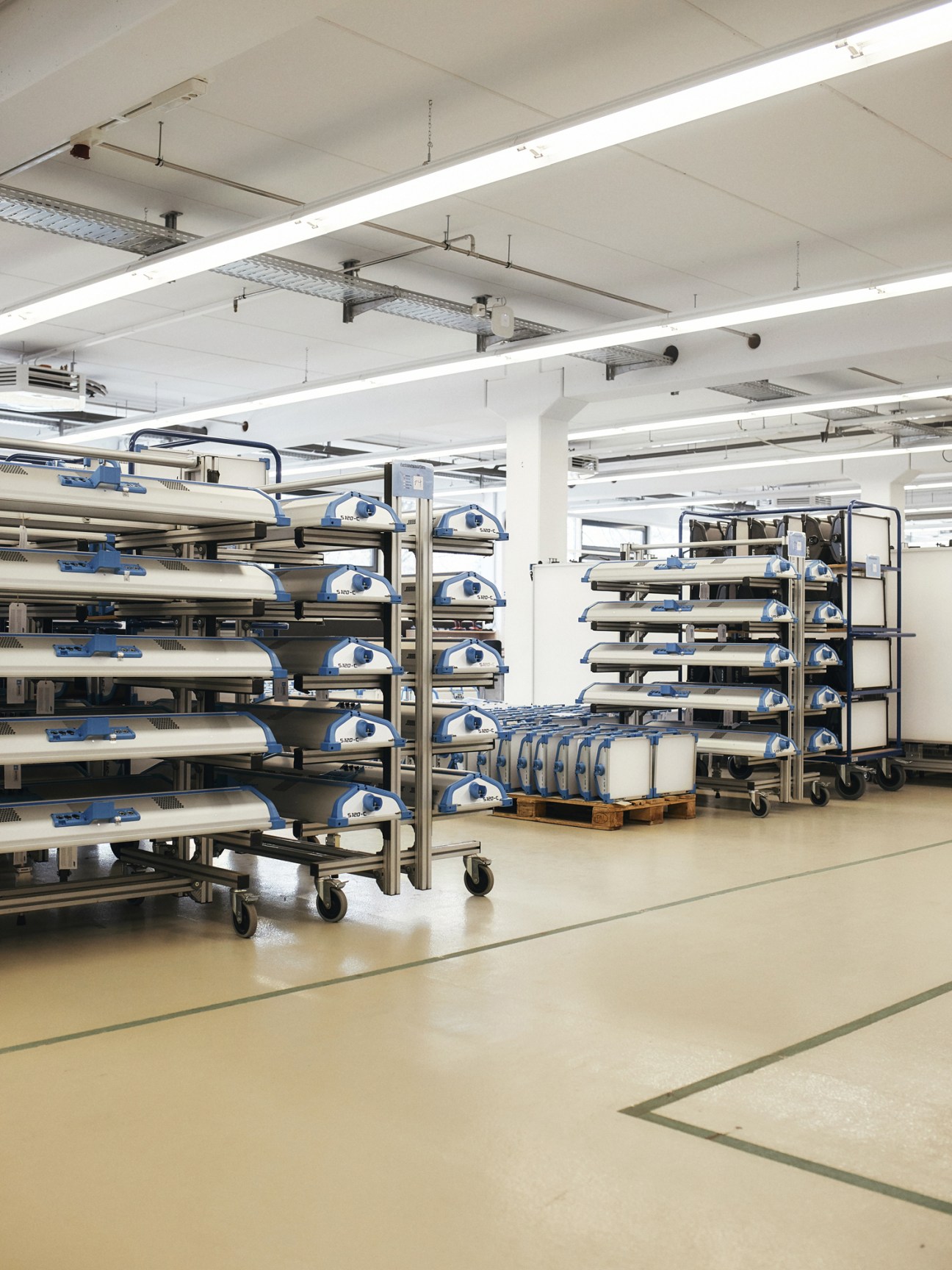 Arri factory floor with metal shelving units holding rolled cylindrical lighting equipment marked with blue bands.