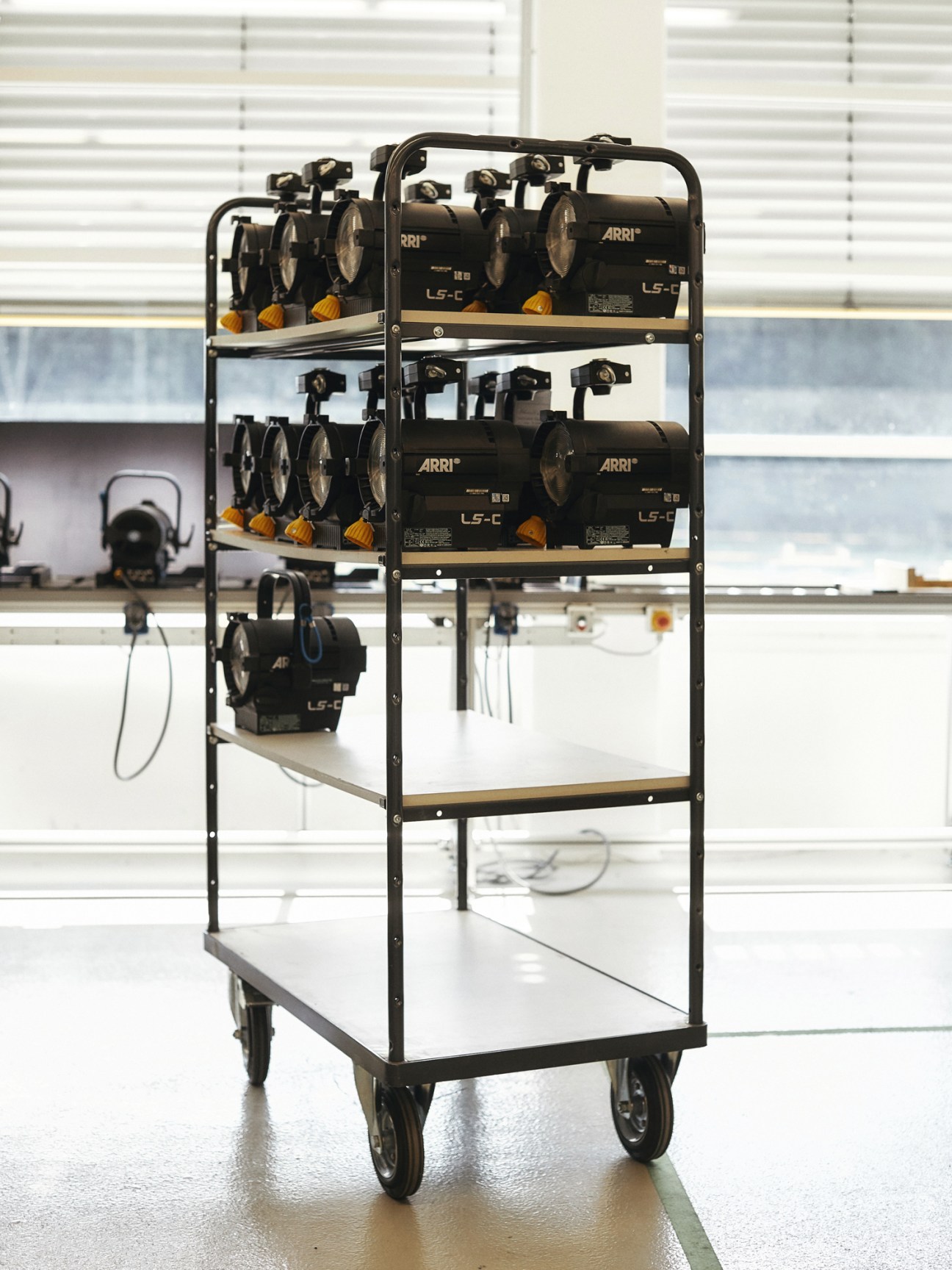 Mobile shelving unit displaying ARRI LS-C spotlights with yellow fixtures on a studio floor.