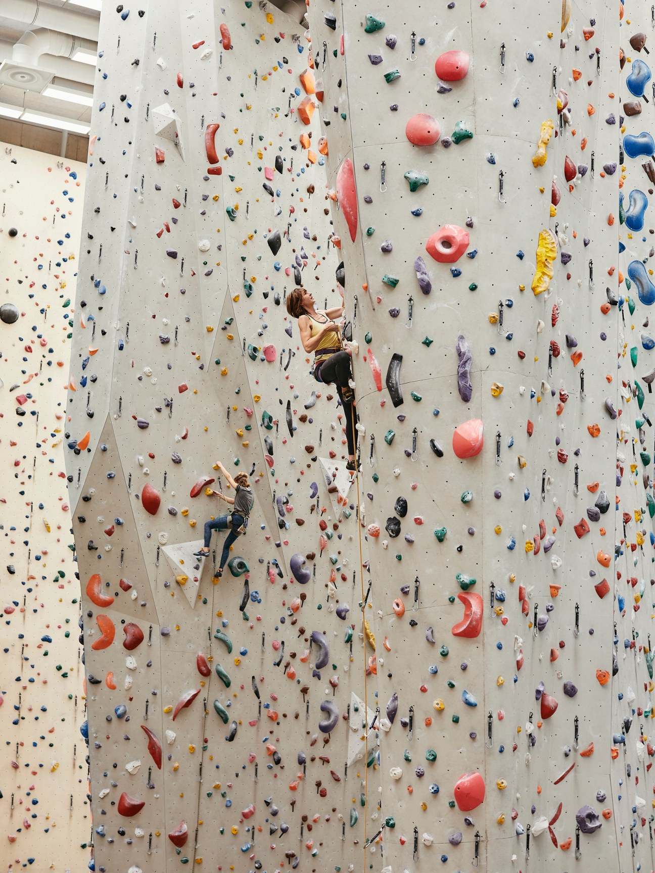 Two climbers scaling a colorful indoor climbing wall with multicolored holds at climbing center