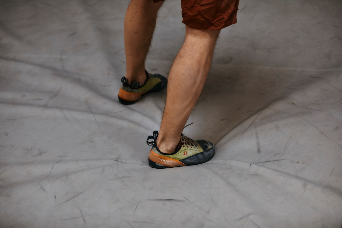 Close-up of climber's feet wearing specialized climbing shoes on white textured surface