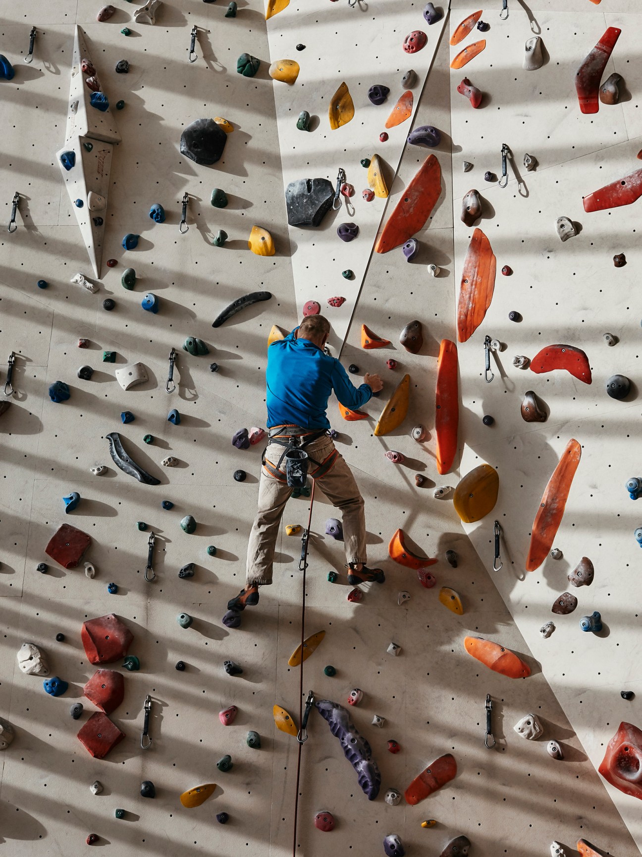 Rock climber in blue shirt scaling an indoor climbing wall with colorful holds