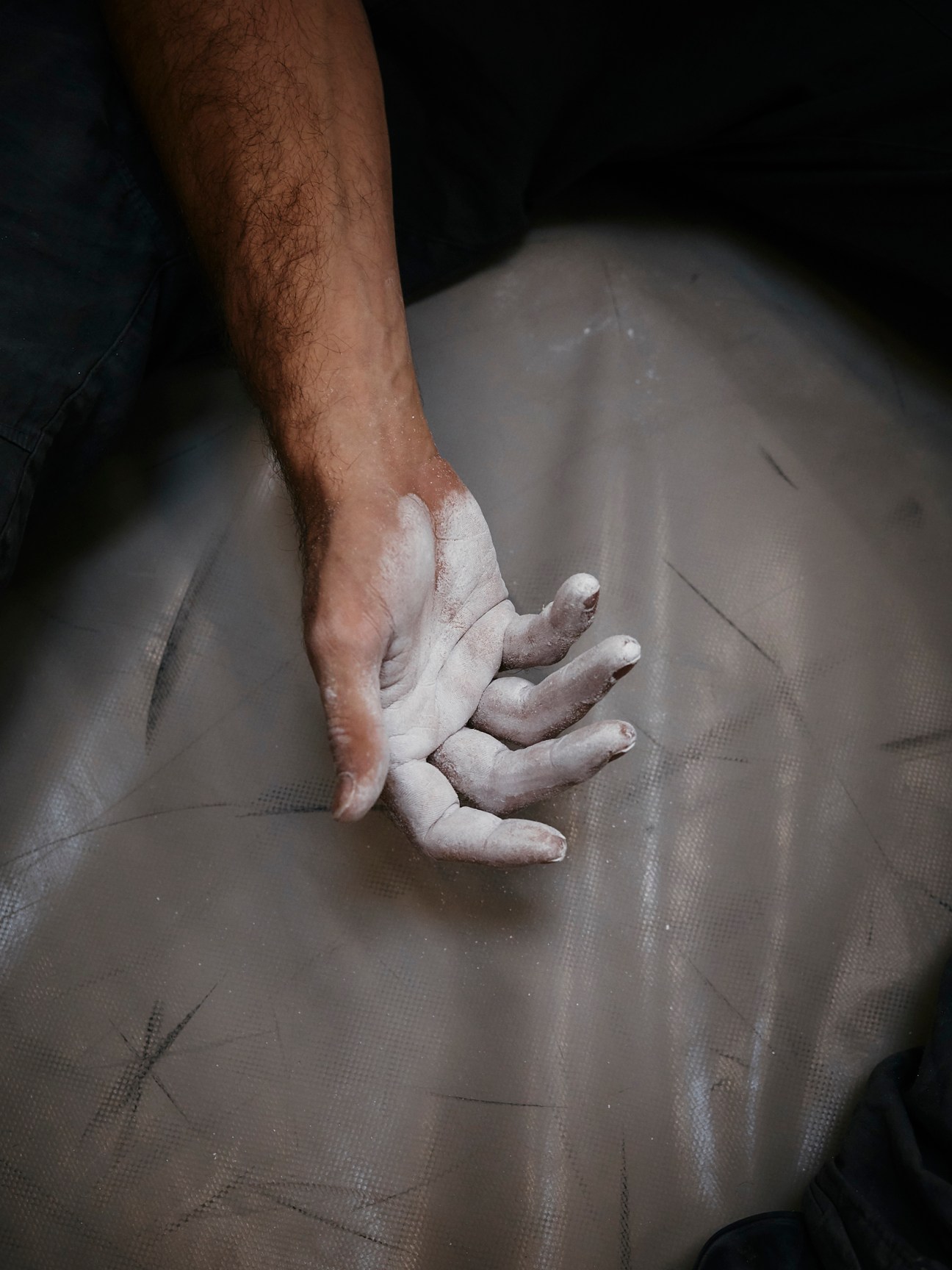 Chalk-covered hand resting on climbing mat at indoor climbing facility