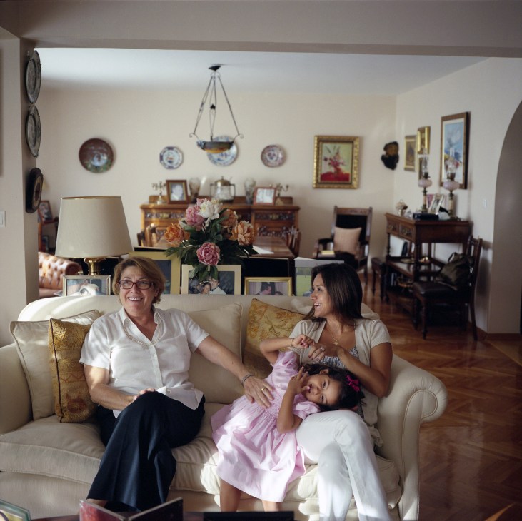 Rosemary, Diana and Leticia Dologh sit together on a cream sofa in an elegantly decorated living room filled with family photos and antique furnishings.