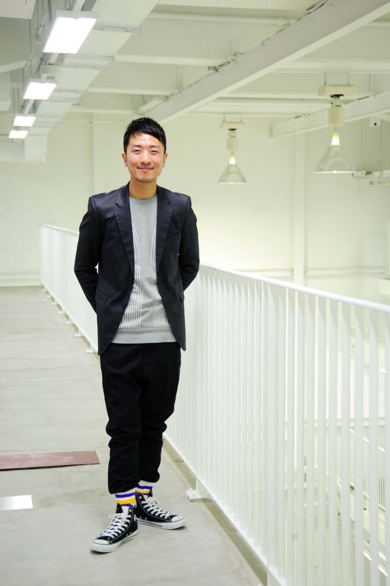 Man in black blazer and grey shirt standing in a bright industrial corridor with white railings.