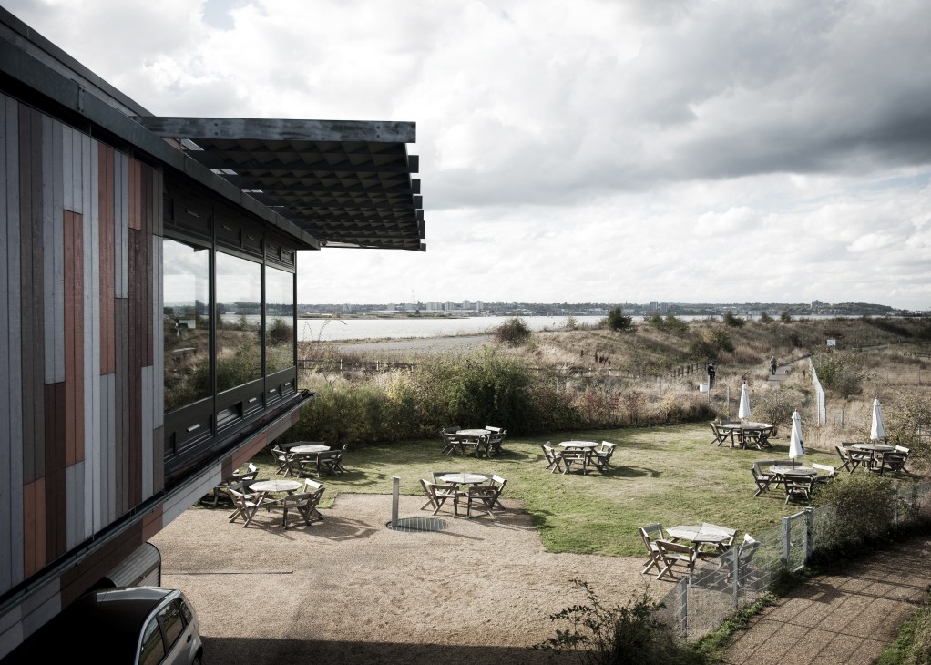 Modern building with cantilevered roof overlooking outdoor seating area and marshland at RSPB Centre, Purfleet.