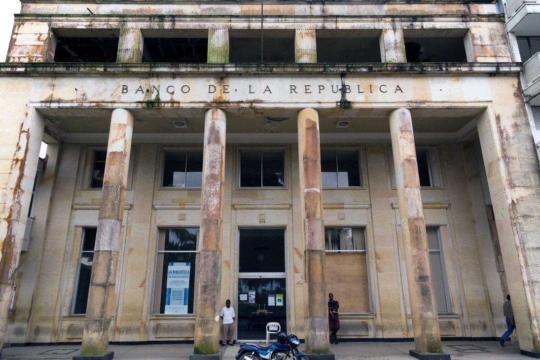 Weathered neoclassical building facade with Banco de la República text, featuring deteriorating columns and boarded windows.