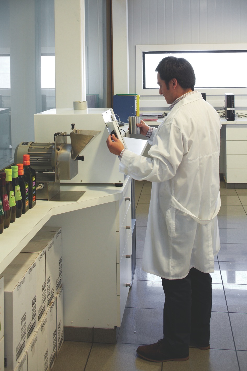 Man in white lab coat examining olive oil sample in processing facility