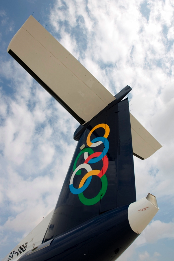 Olympic Air aircraft tail fin displaying the airline's colorful interlocking rings logo against sky.