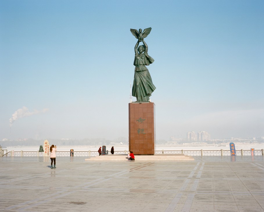 Bronze statue of a woman holding a winged child on a red-brick pedestal on Heihe's waterfront