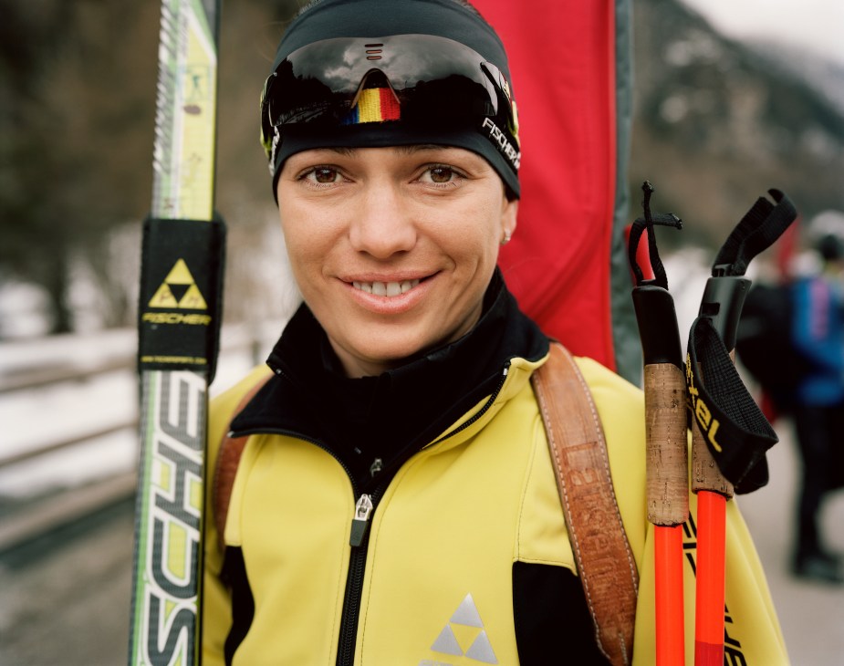 Romanian biathlon contestant in yellow jacket and black headband with skis, smiling at camera.