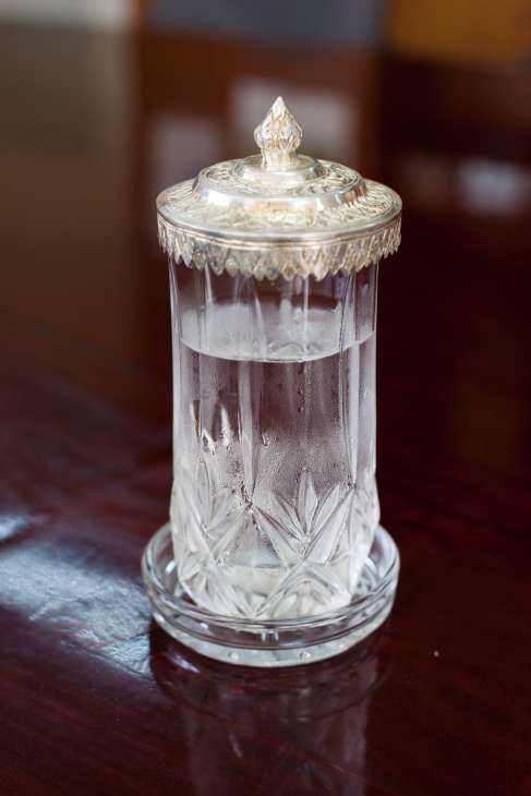 Crystal glass of water with ornate metal lid on dark surface, symbolizing clean water access.