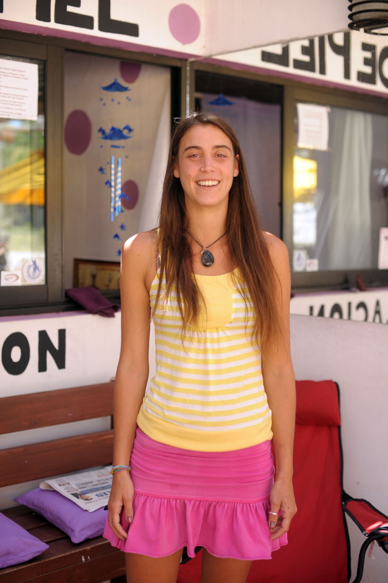 Sur López smiling inside Luna de Piel beauty shop, wearing a yellow and white striped tank top and pink skirt.