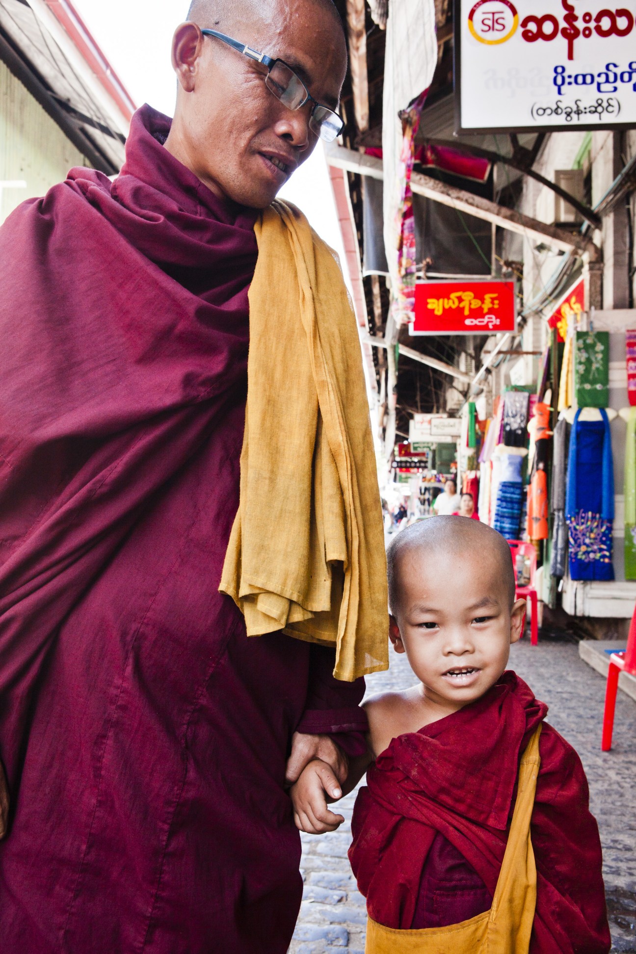 Buddhist monk and young novice holding hands at Scott Market in Rangoon, wearing maroon and yellow robes.