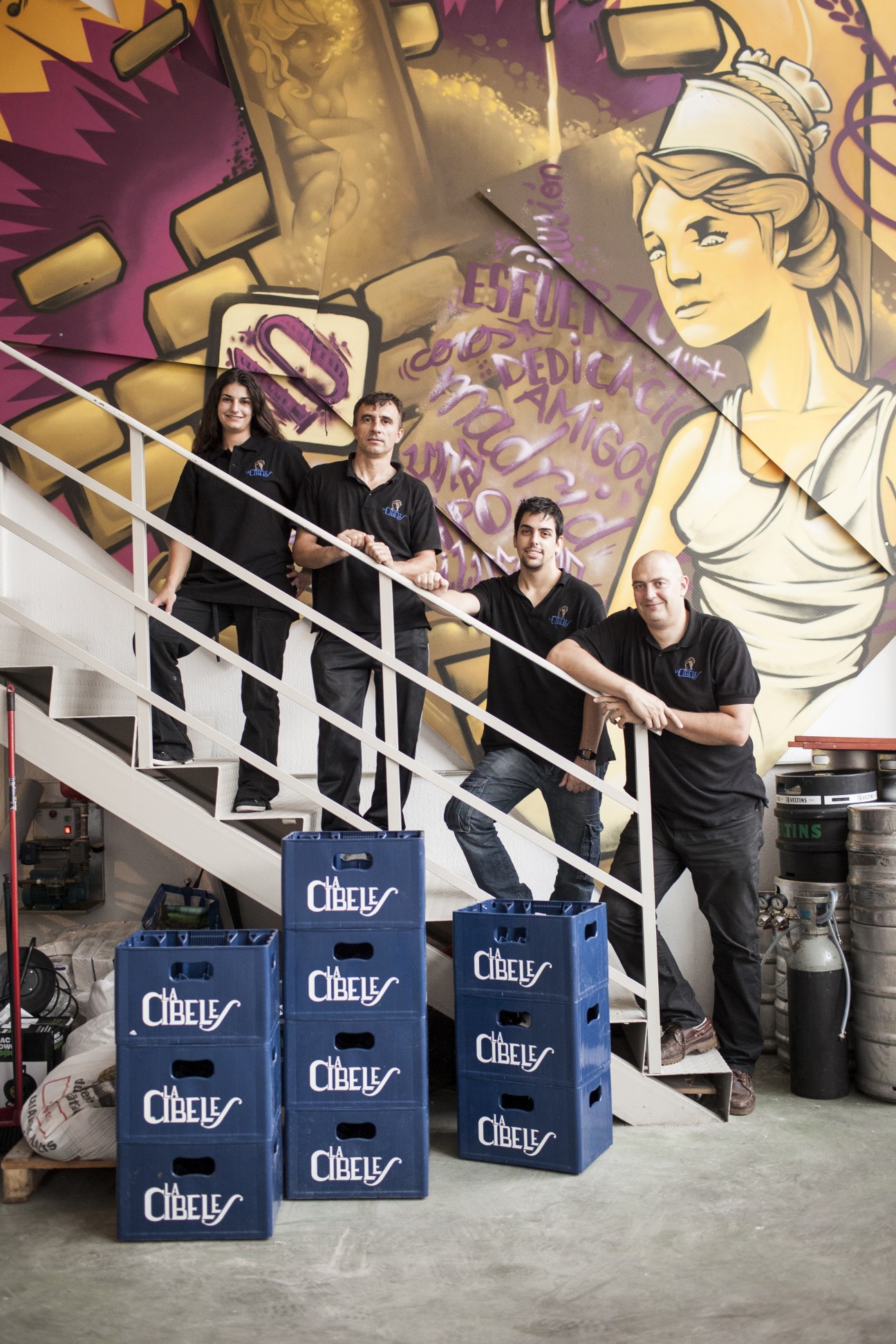 David Castro and his team stand on stairs at their Madrid brewery with Cibeles branded crates below.